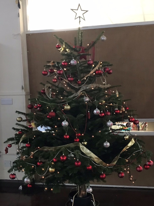 A photo of a christmas tree in a school hall decorated in red and gold
