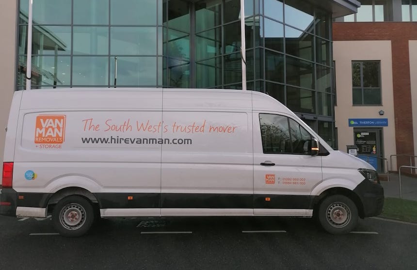 a white van with orange branding parked outside a glass fronted council building and library