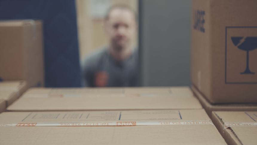 A blurry man in the background and packing boxes in the foreground